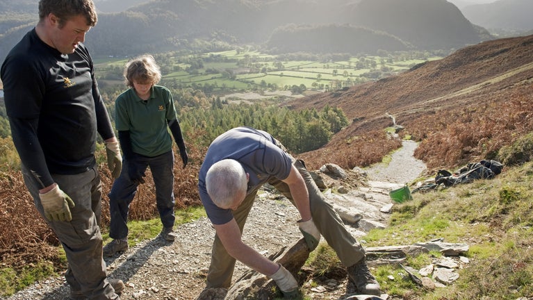 Three volunteers fixing a path up on the fells with a view of the valley below